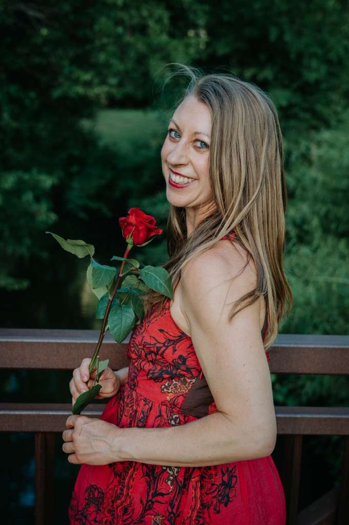 Emily Garnett holding a rose on a bridge surrounded by greenery